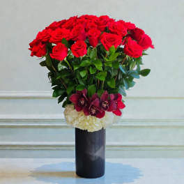 Red roses arranged in a tall black vase with white and burgundy flowers at the base