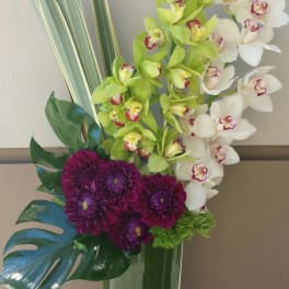 Tall orchid and purple chrysanthemum arrangement in a glass vase