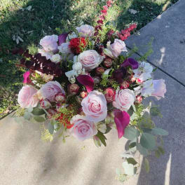 Large arrangement of light pink roses with dark pink calla lilies and mixed blooms outdoors