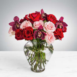 Red roses, pink roses, and purple orchids arranged in a clear glass vase