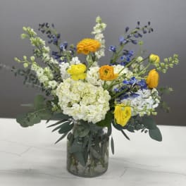 Mixed yellow, white, and blue flowers arranged in a glass vase