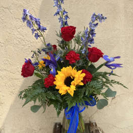 Bouquet of red roses, sunflowers, and blue flowers in a glass vase