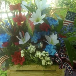 Red, white, and blue floral arrangement in a wooden crate with ribbon