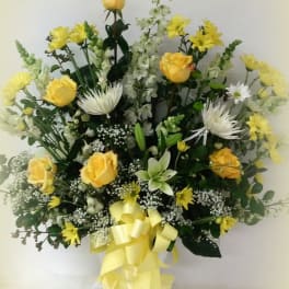 Yellow roses and white flowers arranged in a vase with a yellow ribbon
