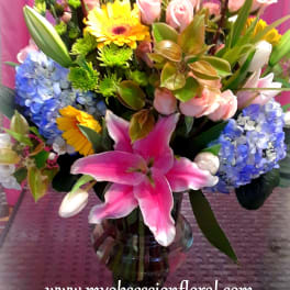 Mixed bouquet in a glass vase with pink lilies, roses, hydrangeas, and yellow daisies