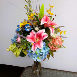 Colorful bouquet with pink lilies, hydrangeas, and yellow accents in a glass vase