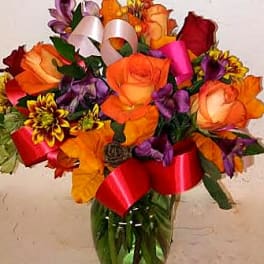 Bouquet of orange, red, and purple flowers in a glass vase with ribbons