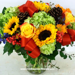 Bouquet of sunflowers, yellow roses, and green hydrangeas in a glass vase with red ribbon