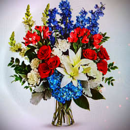 Bouquet of red roses, white lilies, and blue flowers in a clear vase