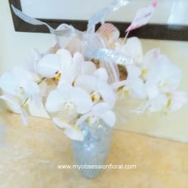 White orchid arrangement in a clear glass vase with ribbon