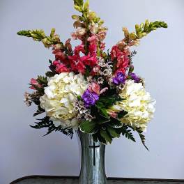 Tall floral arrangement in a silver vase with white, pink, and purple blooms