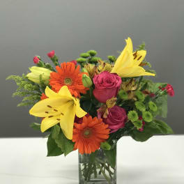 Bouquet of yellow lilies, orange gerberas, and pink roses in a glass vase