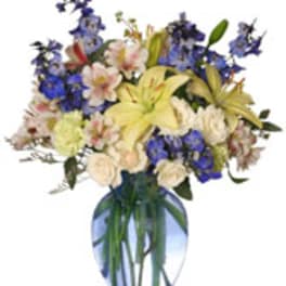 Mixed bouquet of lilies, roses, and blue flowers in a glass vase