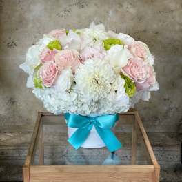 Pink and white flower arrangement in a white box with a blue ribbon