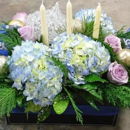 Blue hydrangeas and lavender roses arranged with candles and ornaments in a box