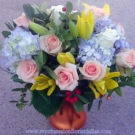 Bouquet of pink roses, yellow lilies, and blue hydrangeas in a vase
