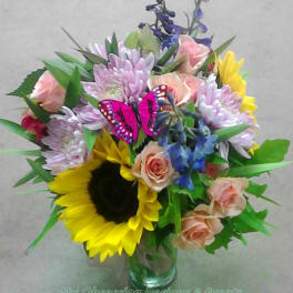 Mixed bouquet with sunflowers, roses, and purple blooms in a glass vase