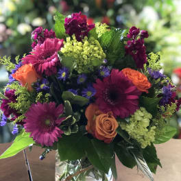 Mixed bouquet of magenta, orange, and purple flowers in a glass vase