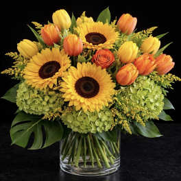 Bouquet of sunflowers, orange tulips, and a rose in a glass vase