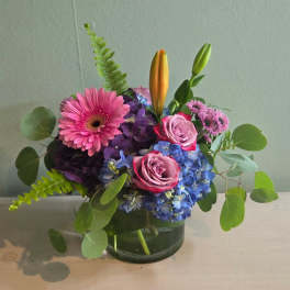 Pink gerbera, roses, blue hydrangea, and lilies in a glass vase