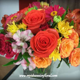 Mixed bouquet of roses, daisies, and orange blooms in a glass vase