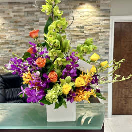 Tall mixed bouquet with green orchids, purple orchids, and roses in a white vase