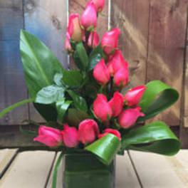 Pink rose bouquet in a square glass vase with broad leaves