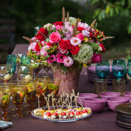 Large pink and red floral centerpiece on a table with glassware and desserts