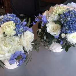 Two white and blue floral arrangements in ribbed white containers