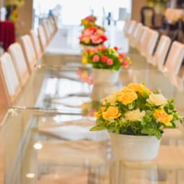 Flower centerpieces in white pots on a long table with white chairs