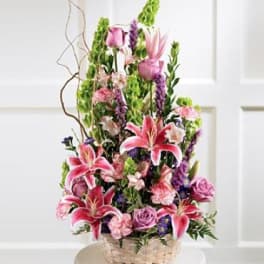 Tall basket arrangement of pink lilies and roses with purple accents