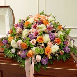 Large floral casket spray with orange roses, pink lilies, and purple blooms