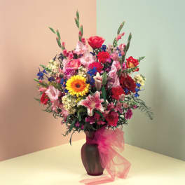 Mixed bouquet of colorful flowers in a dark vase with pink ribbon