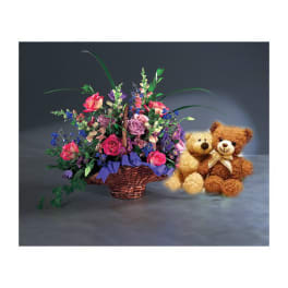 Basket of mixed flowers with two teddy bears beside it