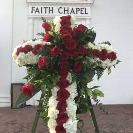 Large cross-shaped floral tribute with red roses and white flowers on an easel