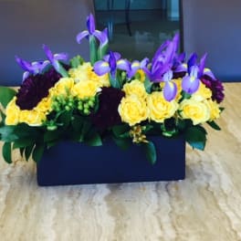 Yellow roses and purple irises arranged in a rectangular vase