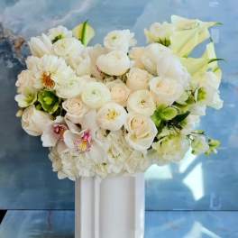 White floral arrangement in a tall white vase with calla lilies and roses