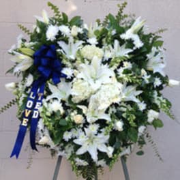 White sympathy wreath with lilies and a blue ribbon reading "Loved"