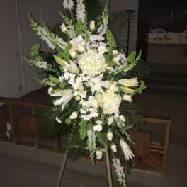 Tall white funeral spray on an easel with lilies and roses