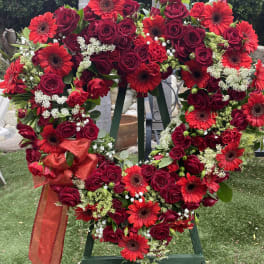 Heart-shaped wreath of red roses and gerbera daisies with a red ribbon
