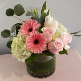Pink gerbera daisies and roses in a glass vase with pale hydrangea