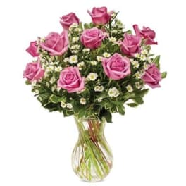 Pink roses arranged with small white flowers in a clear glass vase.