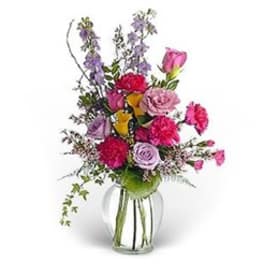 Mixed bouquet of pink, purple, and yellow flowers in a clear glass vase