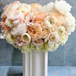 Pastel peach and white roses and ranunculus arranged in a white ceramic vase