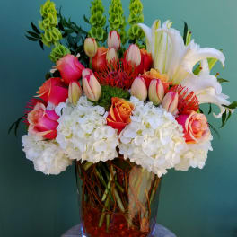 Mixed bouquet of roses, lilies, hydrangeas, and tropical blooms in a glass vase