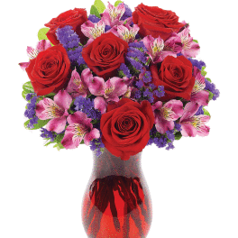 Red roses and pink flowers arranged in a red glass vase