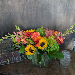 Mixed bouquet of sunflowers, roses, and orchids in a glass vase