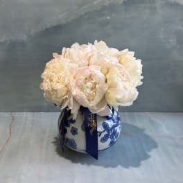 White peonies in a blue-and-white ceramic vase with a ribbon