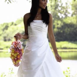Bride in a white gown holding a cascading pink and yellow floral bouquet by a lakeside.