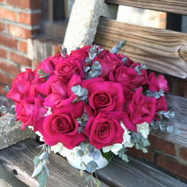 Hot pink rose bouquet in a white container with blue-gray foliage